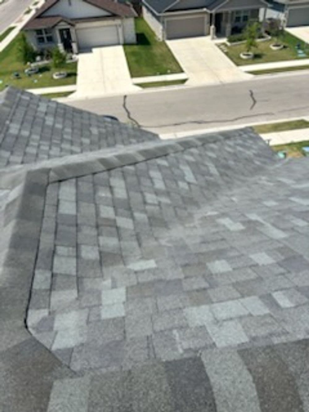 Top view of a gray shingle roof with a sloped design and residential neighborhood background.