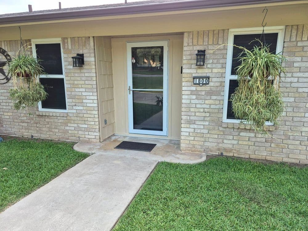 Front entrance of a house with number 1800, featuring hanging plants and a concrete walkway.