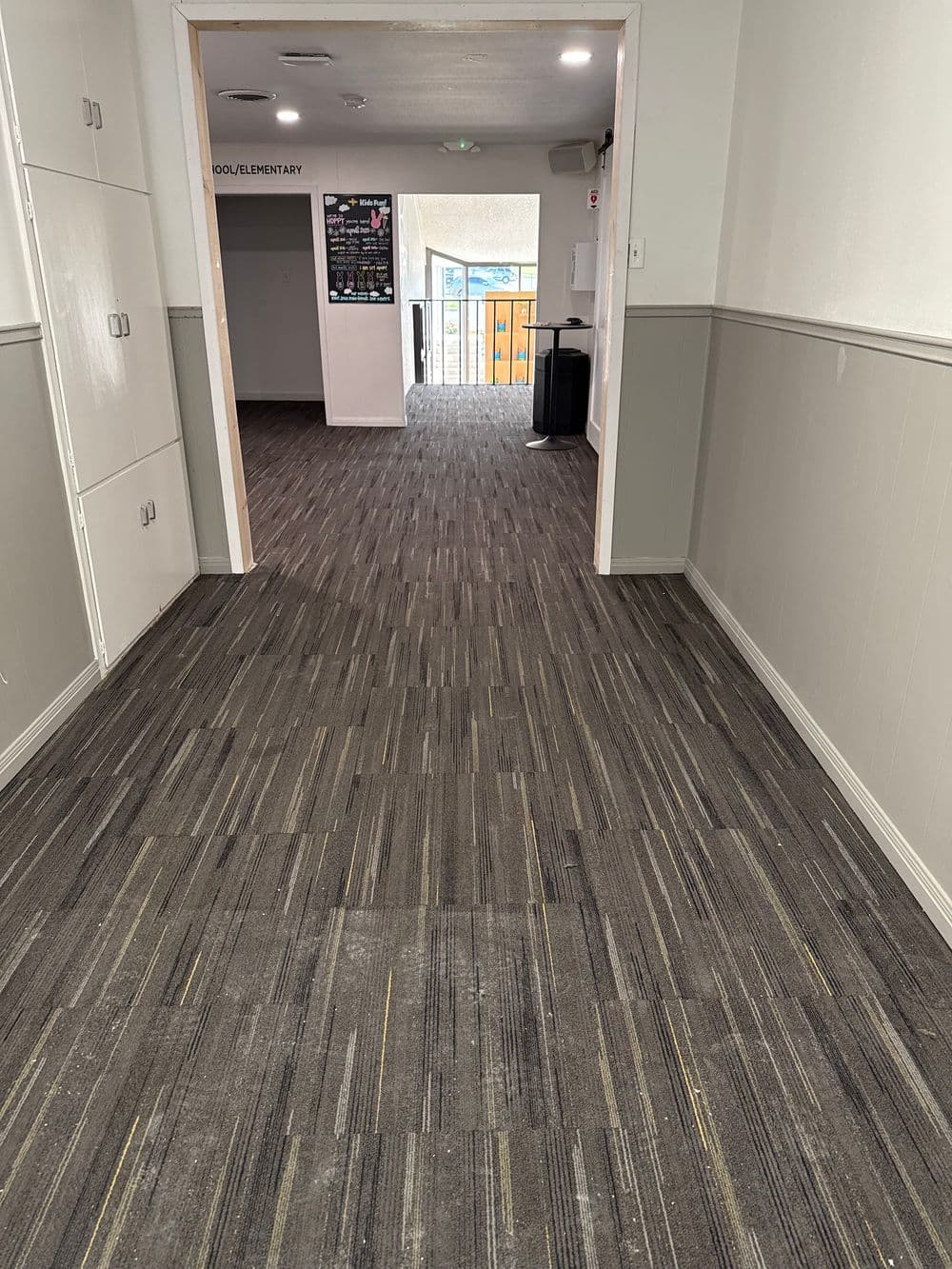 Hallway with modern gray carpet, leading to bright entrance and additional rooms.