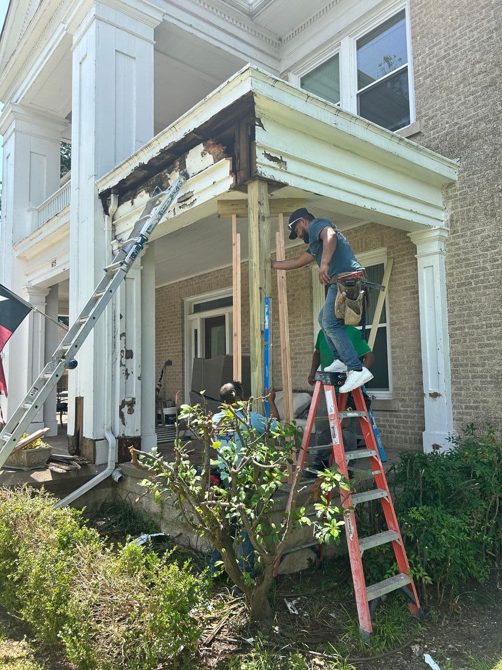 Workers repairing a porch under renovation with ladders and construction tools.