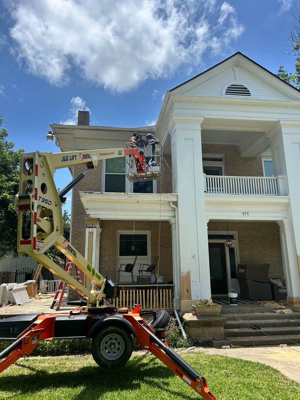Construction workers using a lift for home renovation on a historic house exterior.