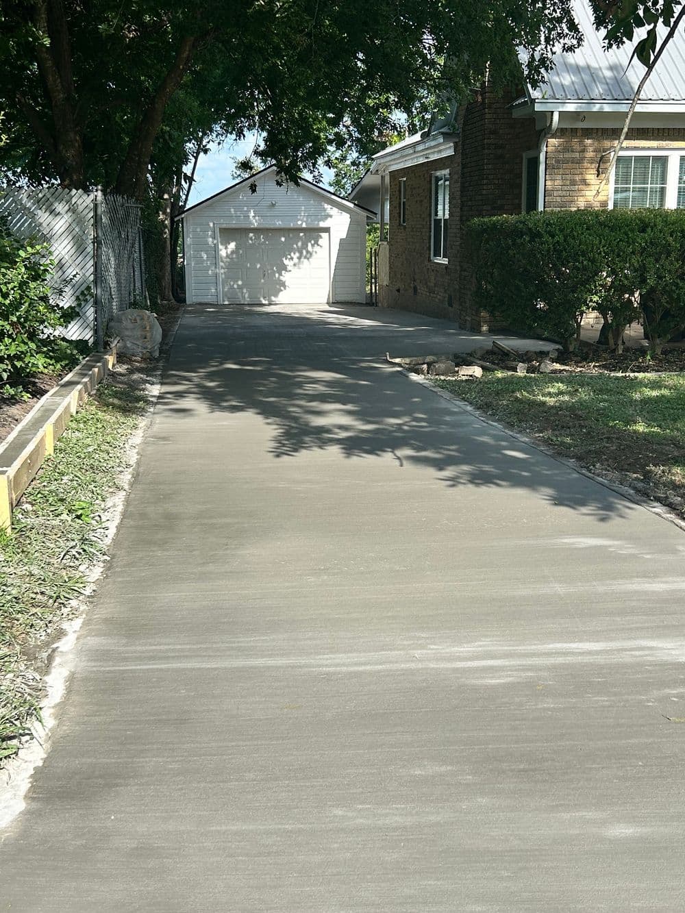 Newly poured concrete driveway leading to a garage beside a brick house.