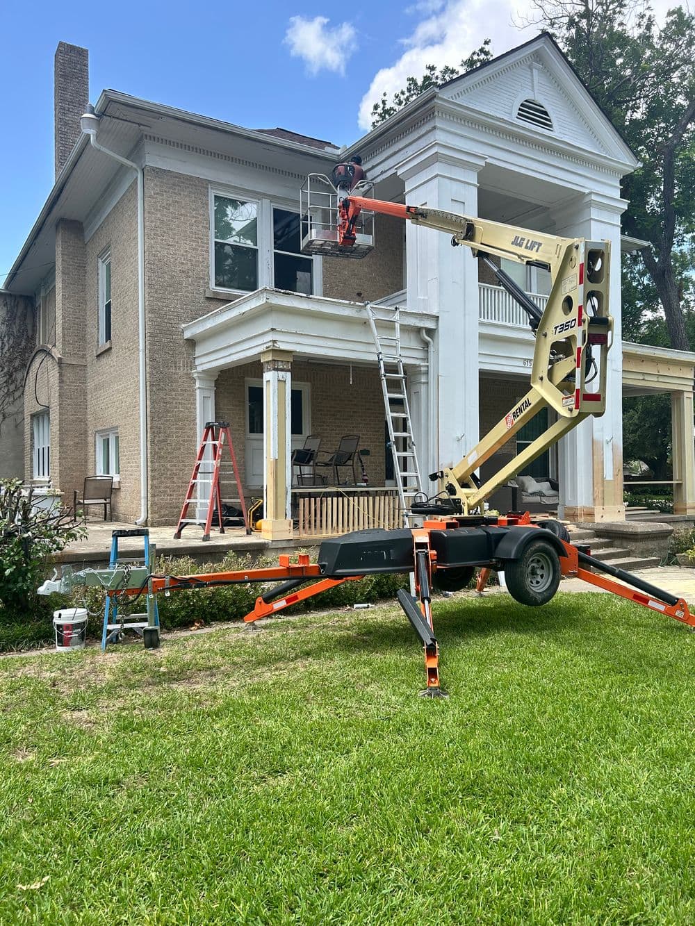 Construction team using a lift to renovate a historic home with ladders and tools nearby.
