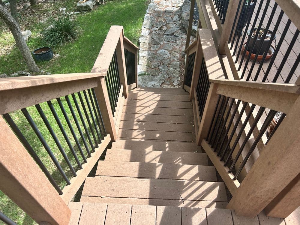 Wooden outdoor stairs with metal railing, leading down to a grassy yard.