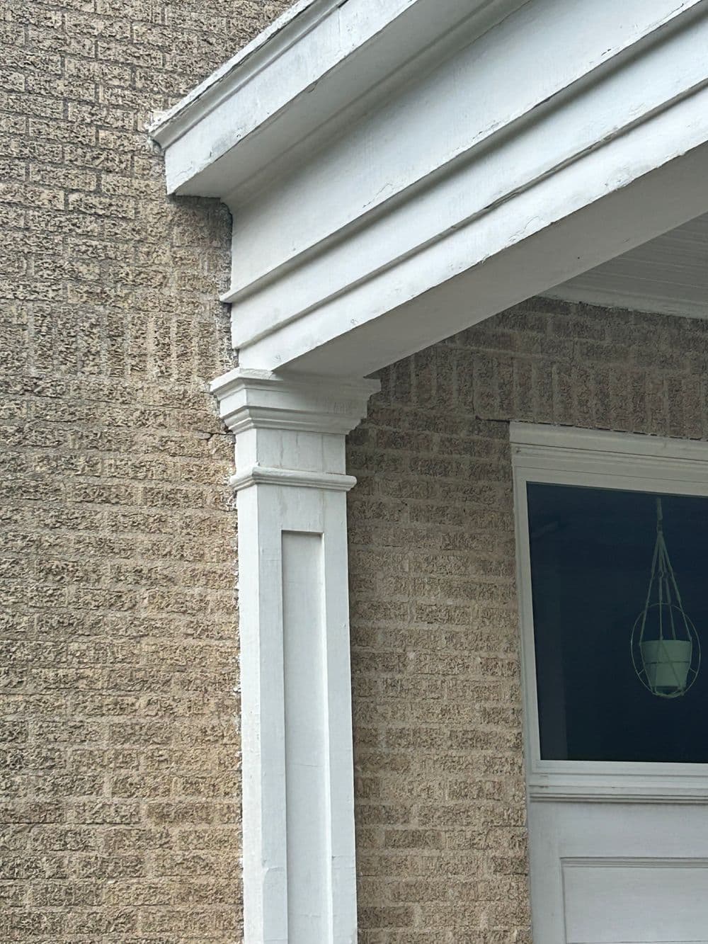 Close-up of a white porch column and textured beige wall of a modern home exterior.