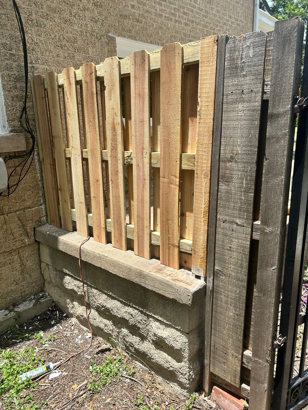Wooden fence with vertical slats on a concrete base, showing unfinished construction details.