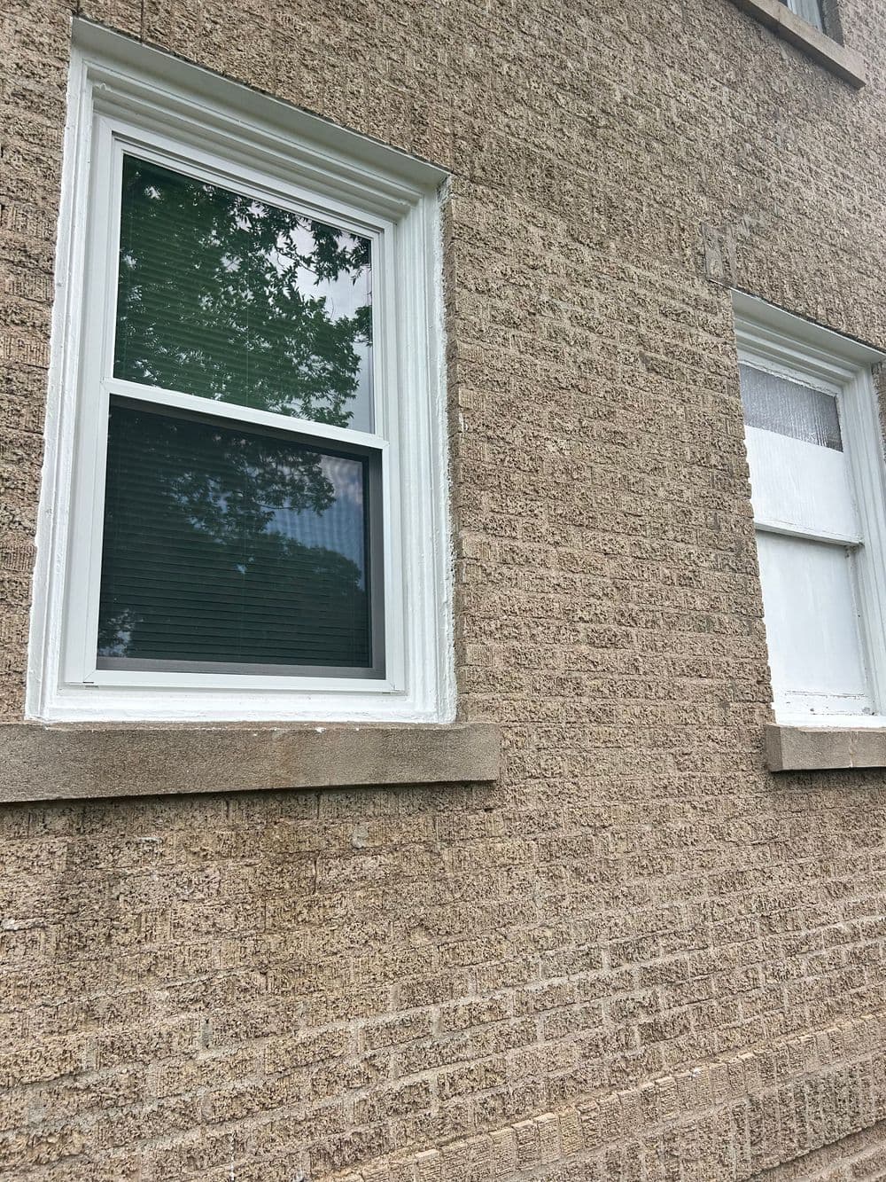 Two windows on a textured brick wall, showcasing white frames and green blinds.