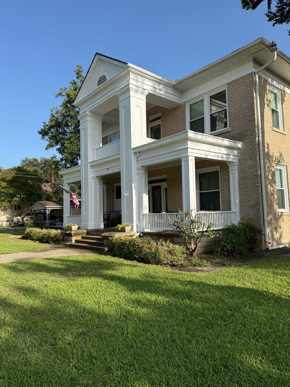 Elegant two-story house with white columns, green lawn, and clear blue sky.
