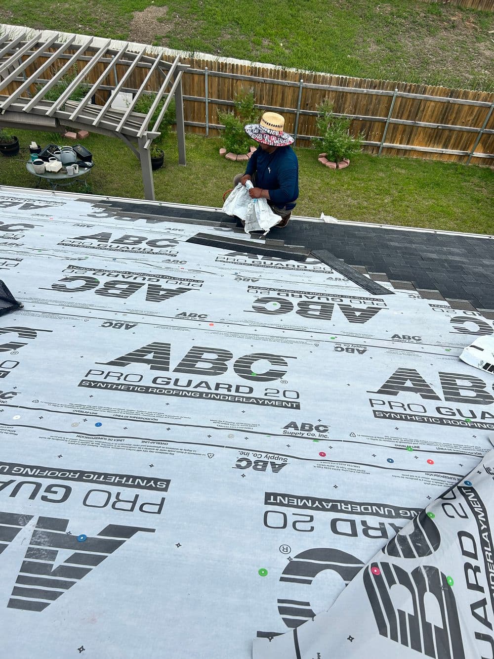 Worker installing ABC Pro Guard 2.0 roofing underlayment on a sloped roof.