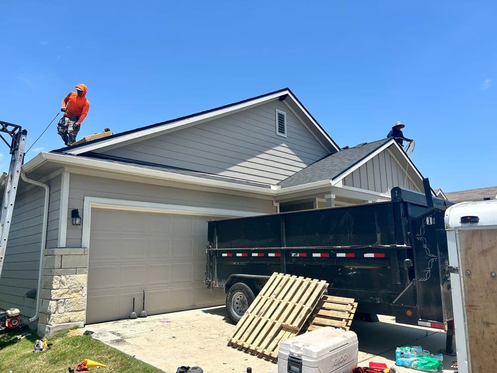 Roofers working on a house renovation with a trailer and tools visible in front.