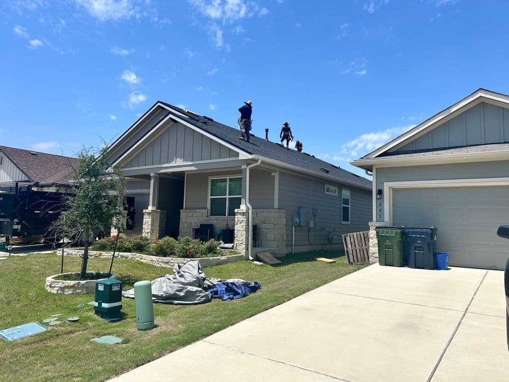 Roofing contractors working on a residential home's roof under a clear blue sky.