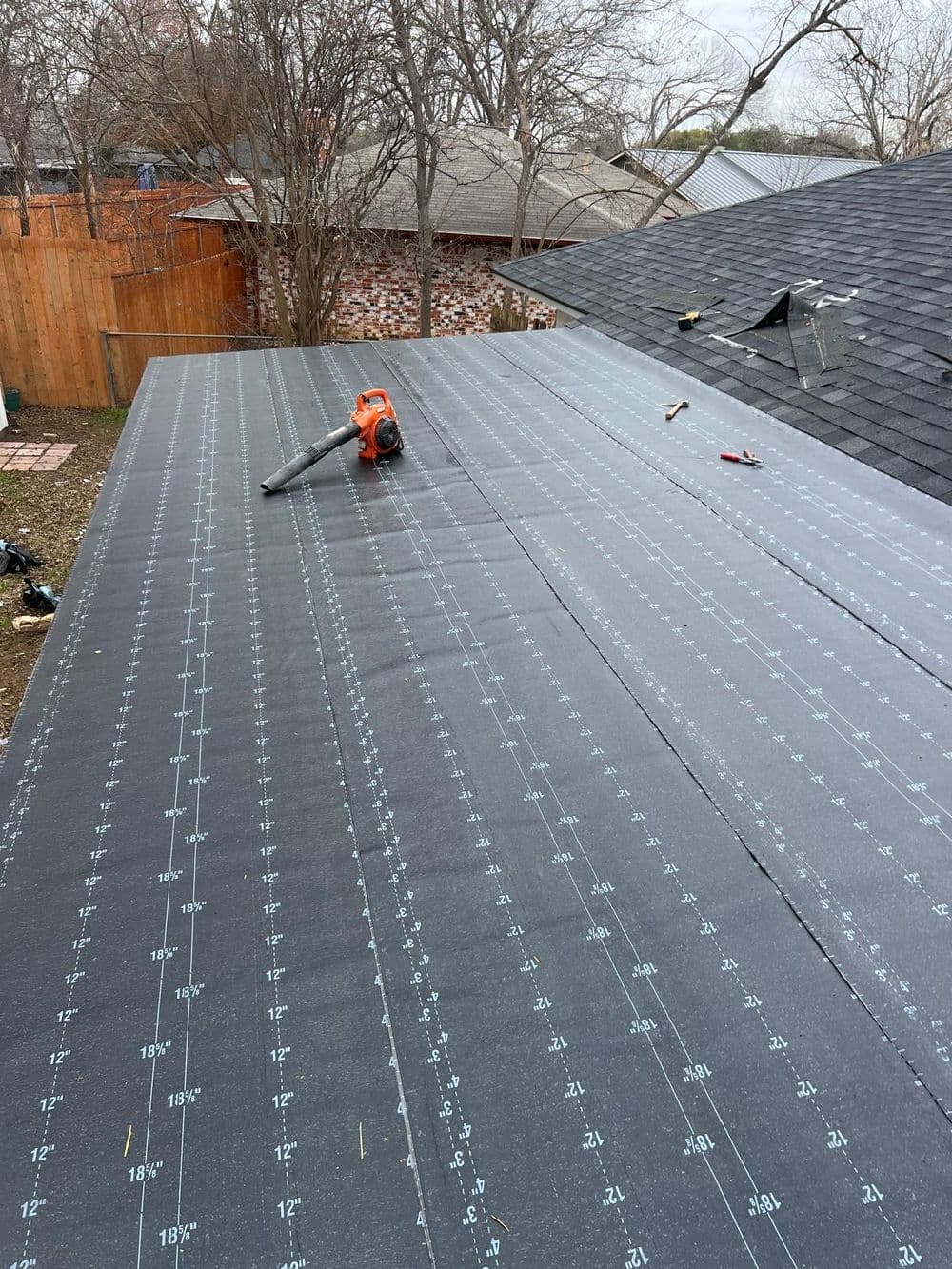 Roofing installation process with marked shingles and a tool on a sloped rooftop.