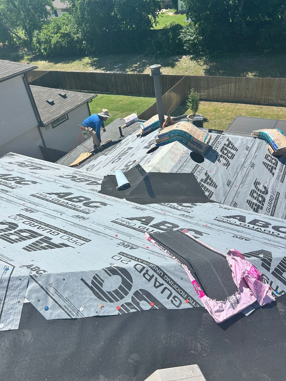 Workers installing roofing material on a residential roof with a clear sky background.