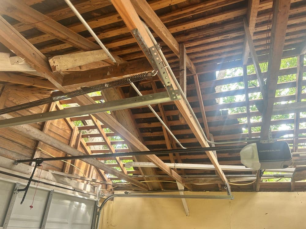 Interior view of a garage with exposed wooden beams, garage door tracks, and natural lighting.