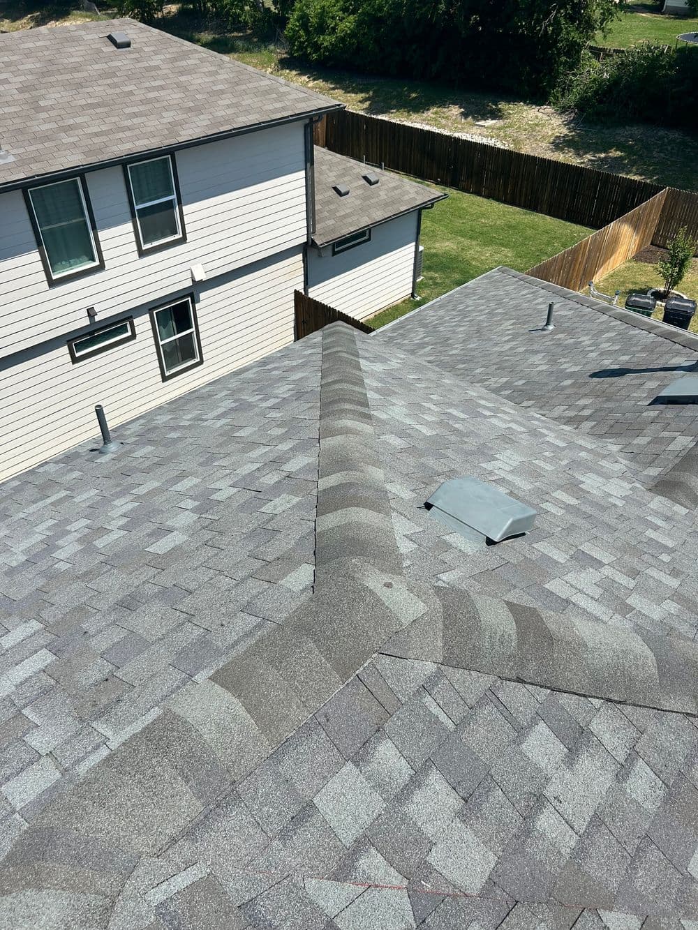 Aerial view of a gray shingled roof with skylight and adjacent houses in a residential area.