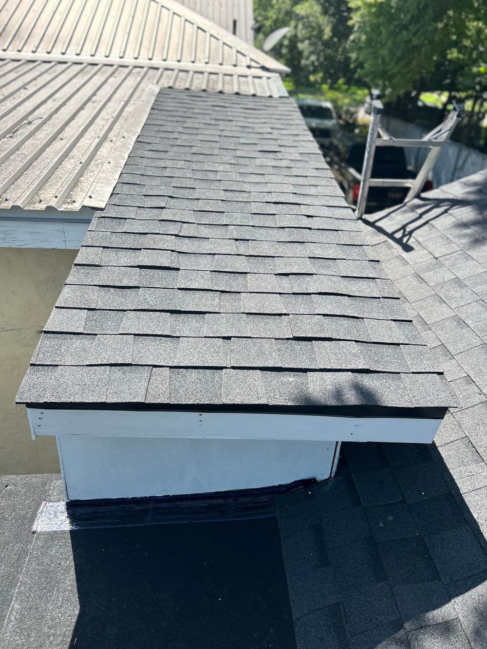 Newly installed black asphalt shingles on a residential roof with a vent.