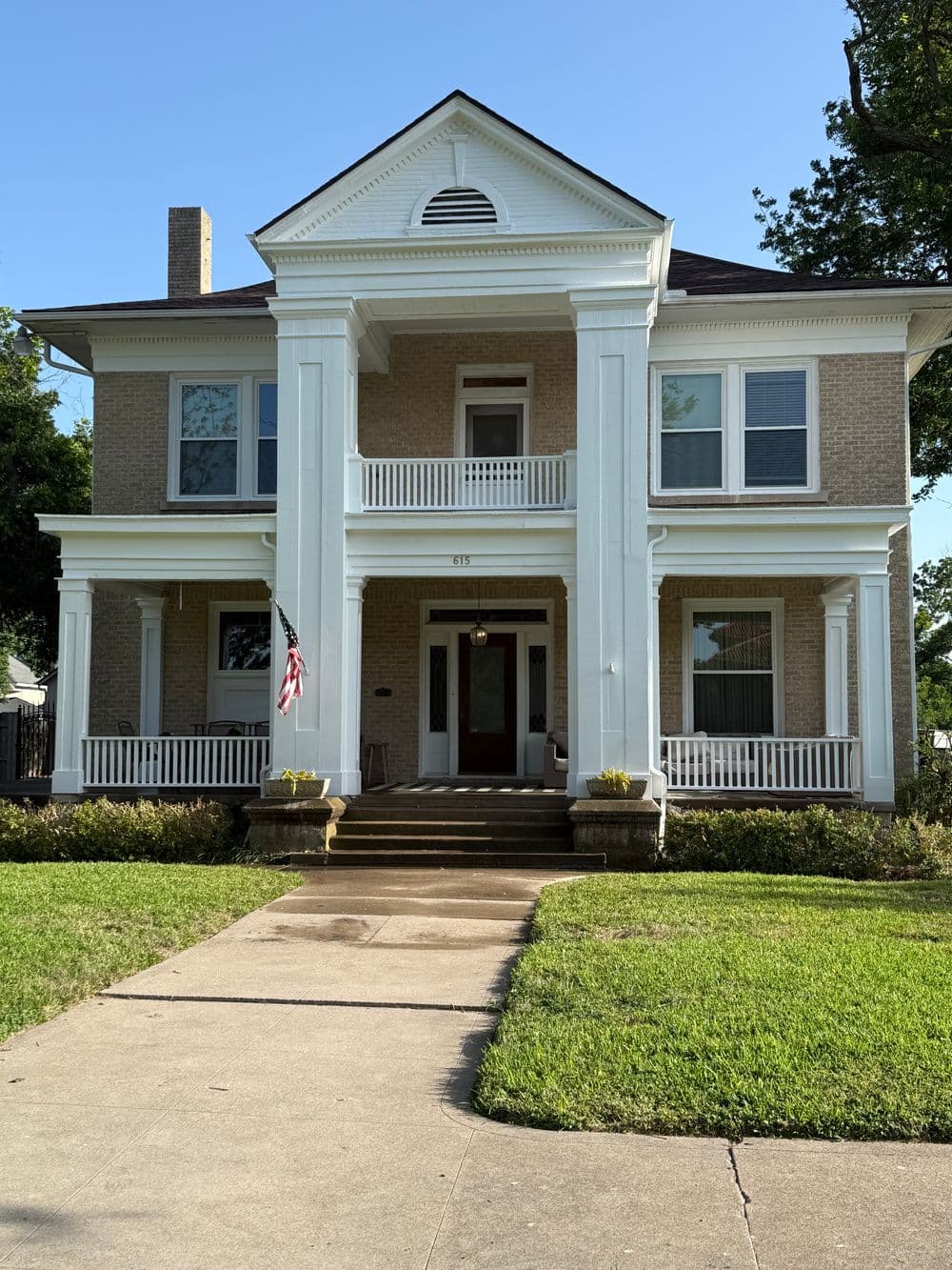 Historic two-story home with white columns, porch, and American flag in front yard.