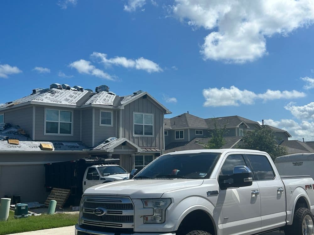 Residential roofing project in progress with trucks and blue sky in background.