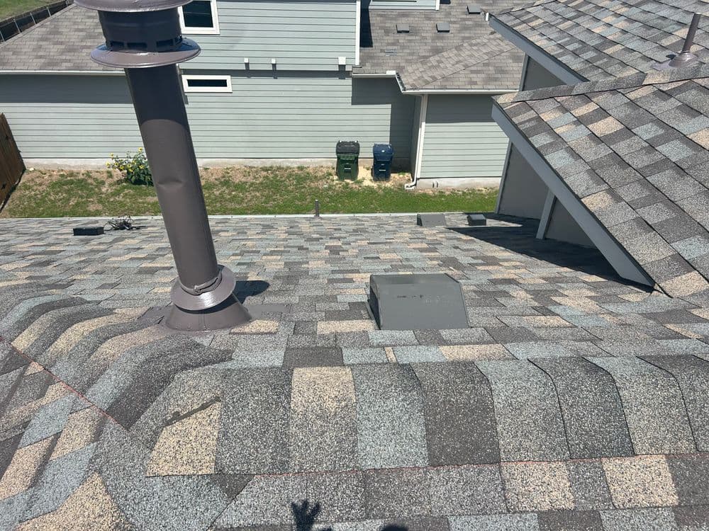 A detailed view of a shingled roof with a chimney and ventilation unit.