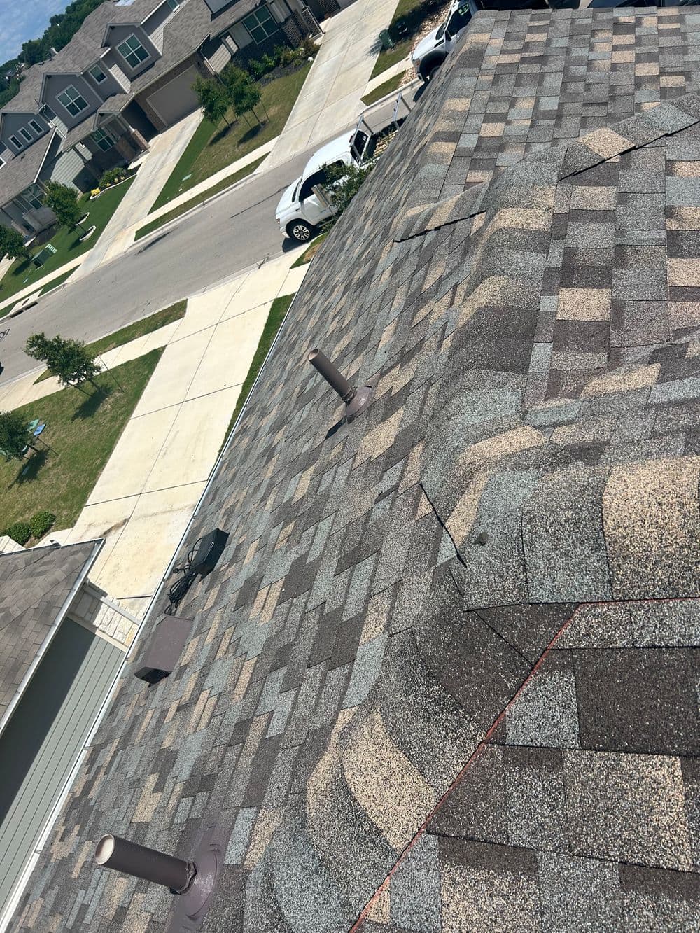 Aerial view of a residential roof with textured shingles and nearby houses in a suburban neighborhood.