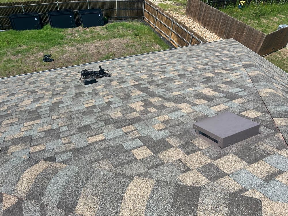 Aerial view of a shingled roof featuring vents and a satellite dish on a sunny day.