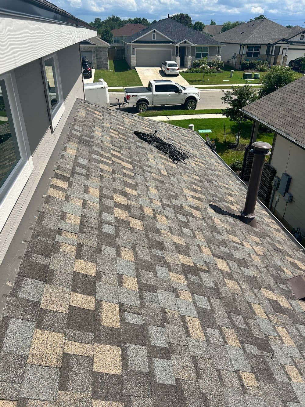 Aerial view of a residential roof with asphalt shingles and a chimney, showcasing neighborhood houses.