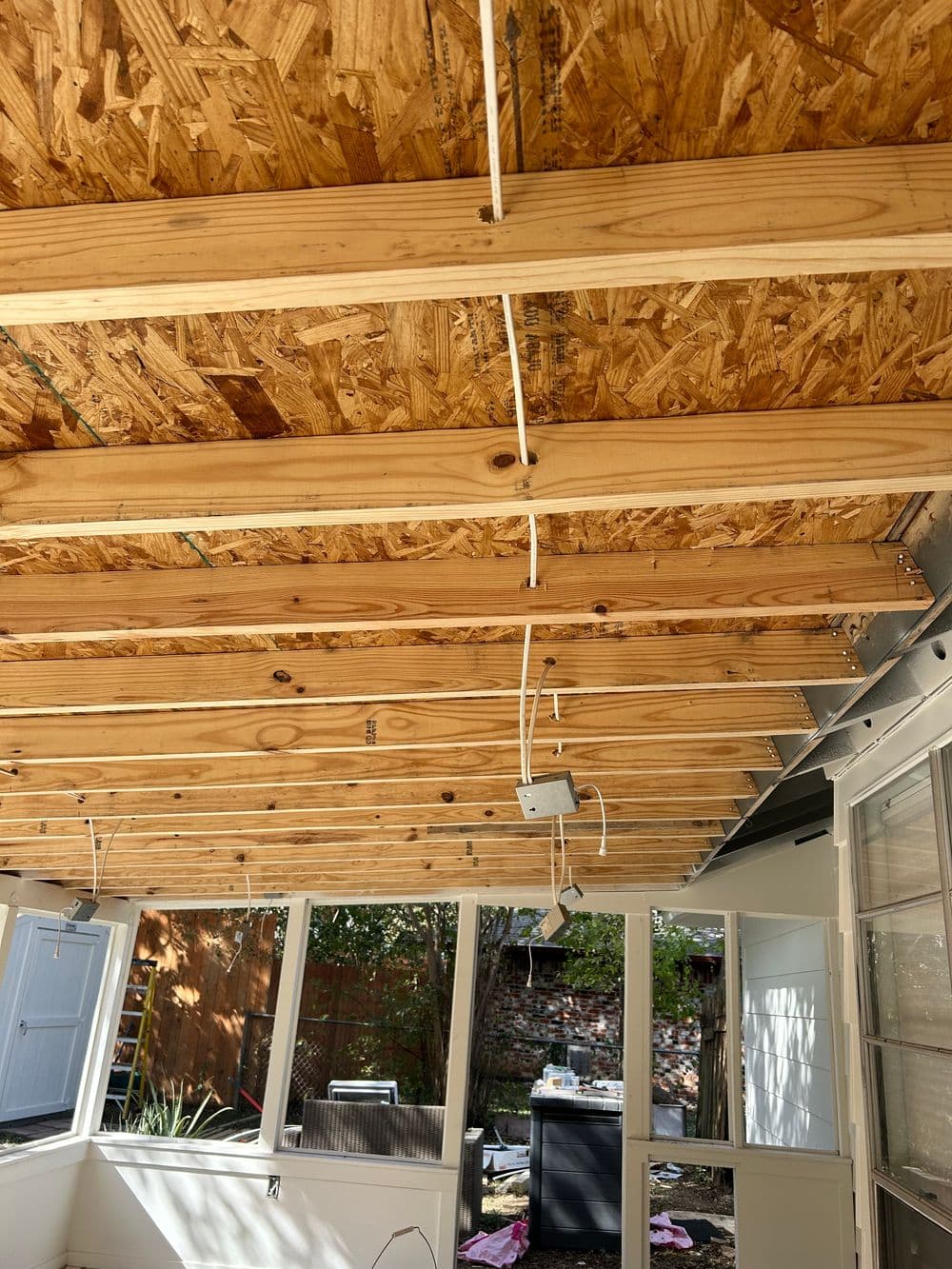 Wooden ceiling beams with exposed electrical wiring in a sunroom renovation.