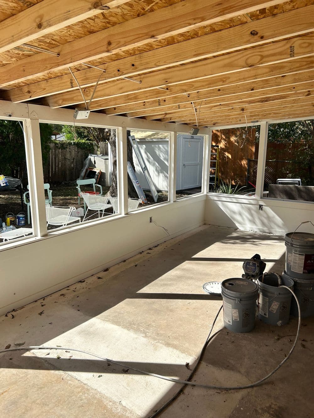 Renovated sunroom with large windows, unfinished concrete floor, and painting supplies.