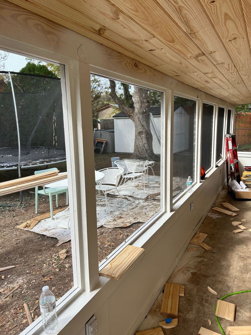 Sunroom with large windows, wooden ceiling, and construction debris, overlooking backyard.