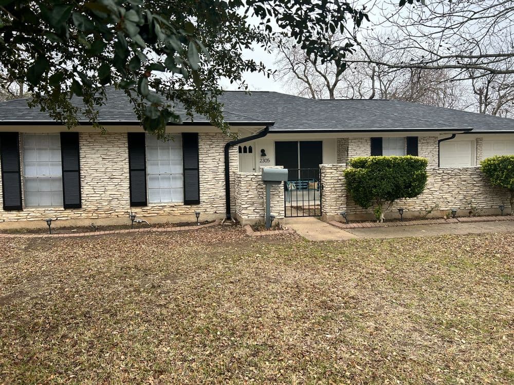 Single-story stone house with black shutters and a well-maintained front yard.