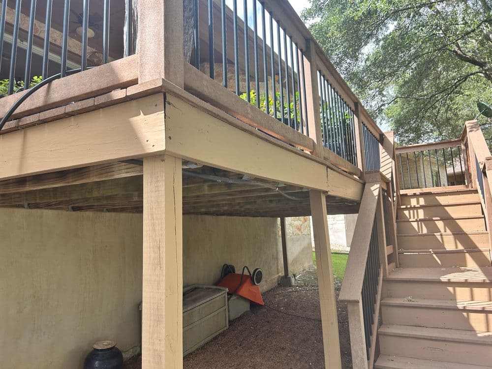 Under-deck storage area and staircase leading to elevated wooden deck with black railings.