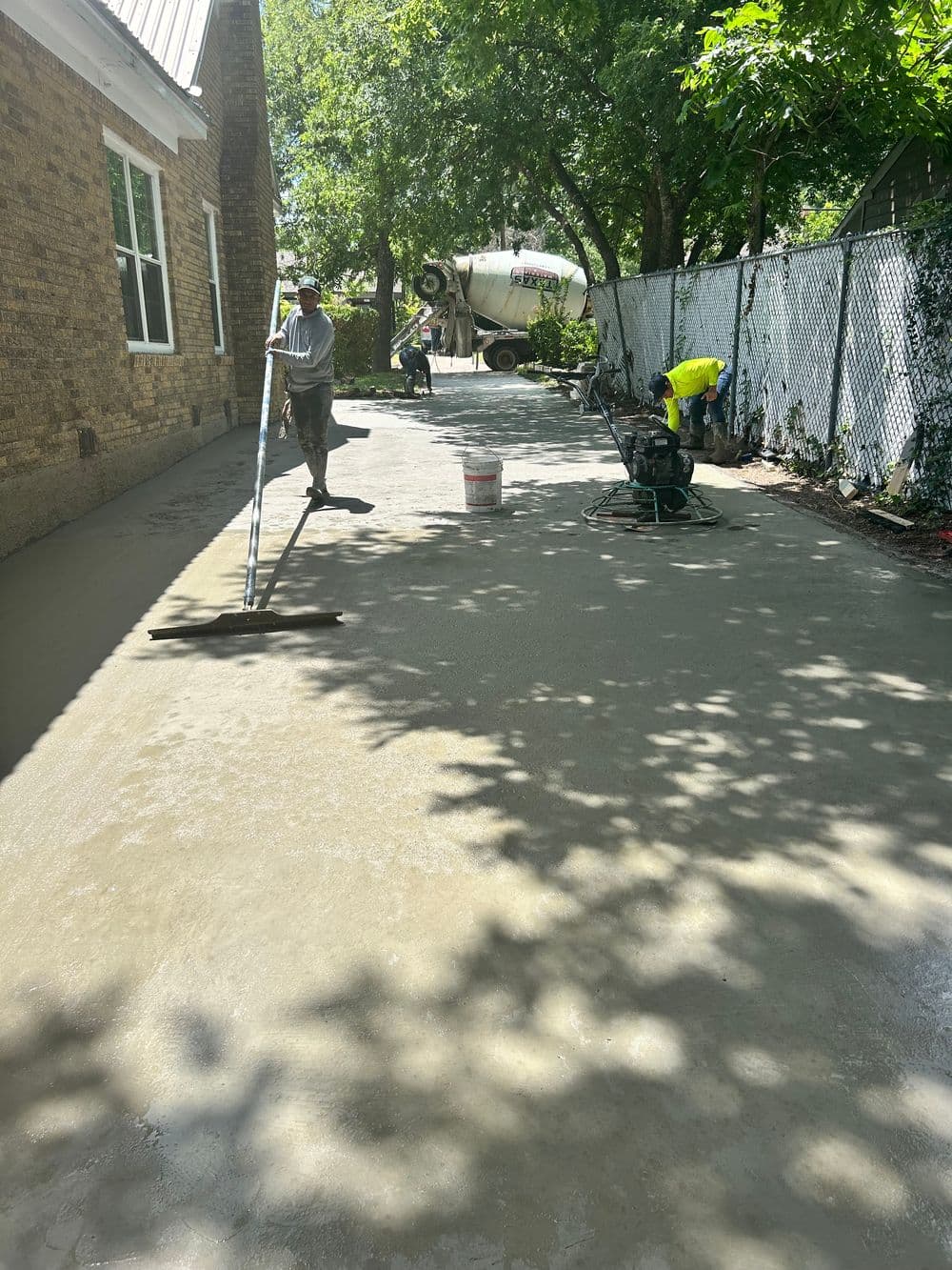 Workers pouring and leveling freshly mixed concrete in a residential outdoor space.