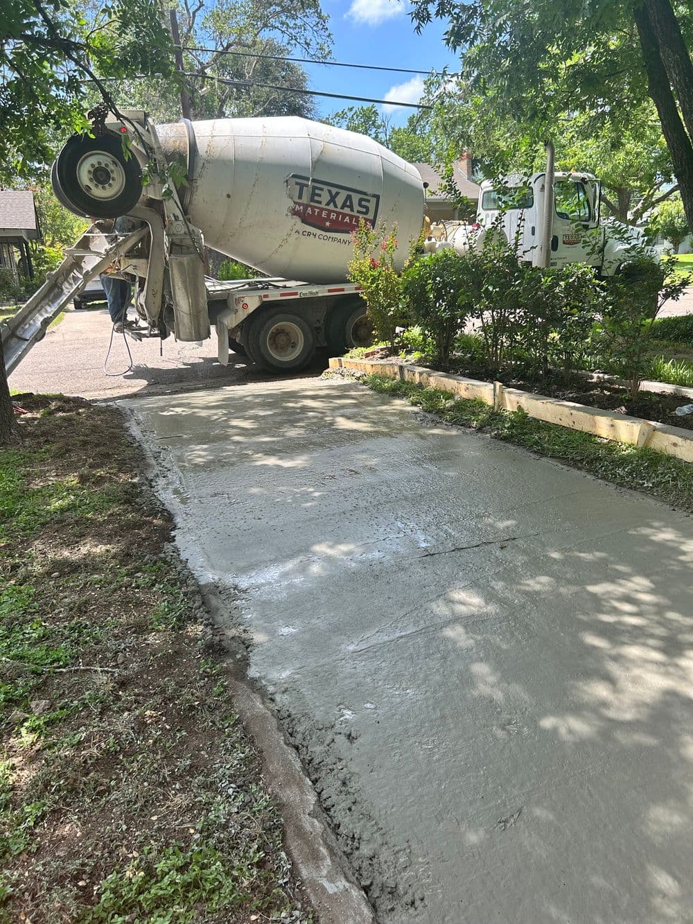 Concrete truck pouring new driveway in residential area surrounded by landscaping.