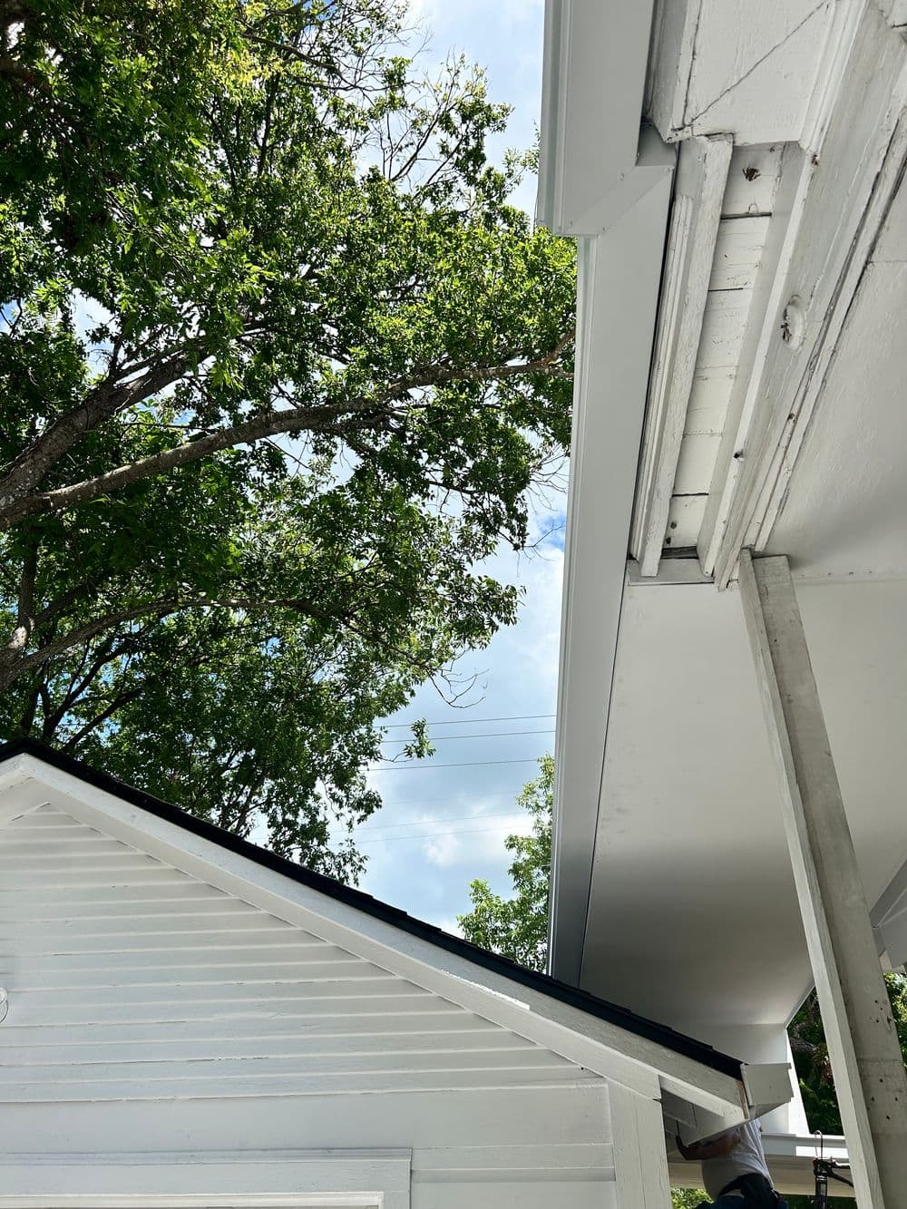 White shed and roofline under a bright sky with green trees in the background.