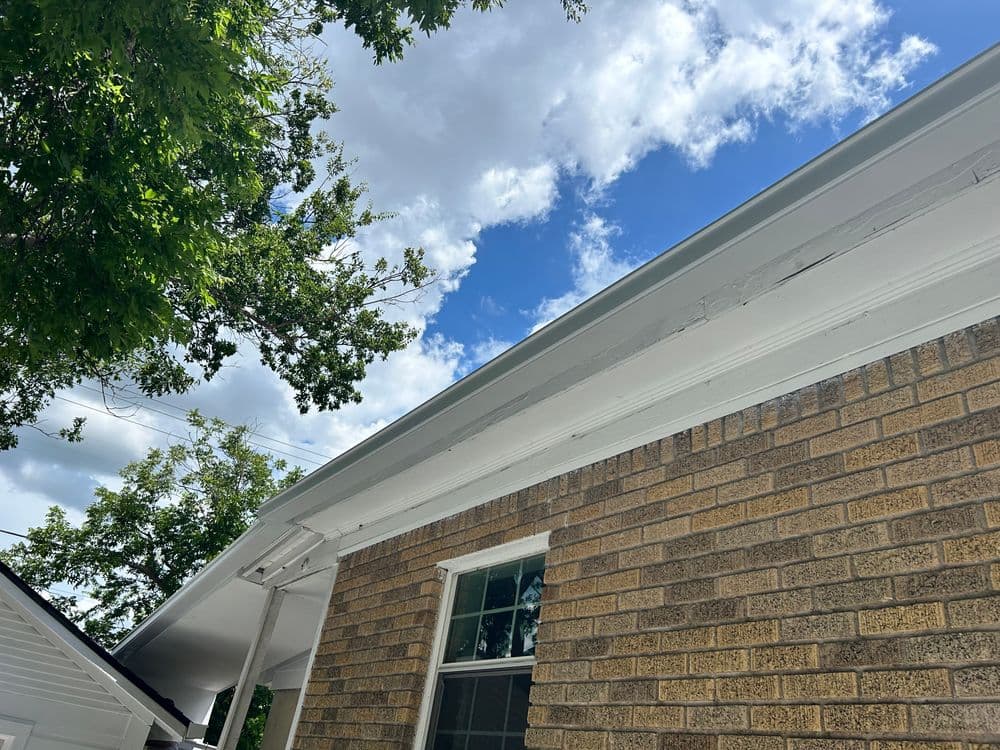 Bright blue sky with fluffy clouds above a brick house and overhanging eaves.