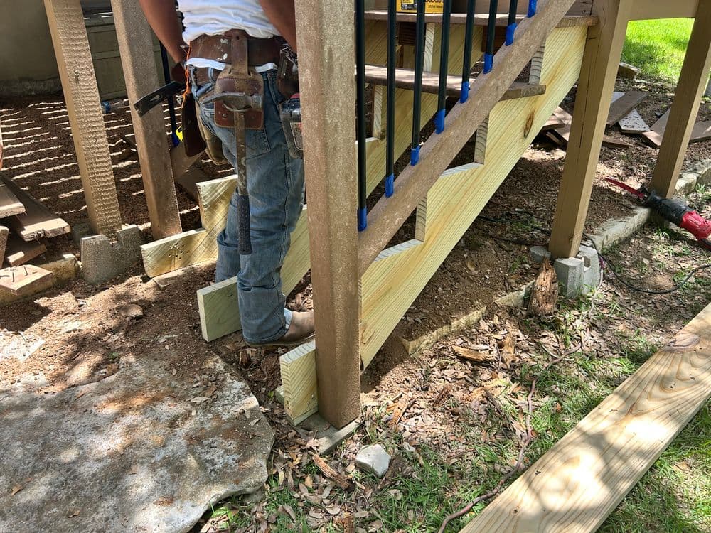 Worker installing wooden stairs with support beams in outdoor construction project.