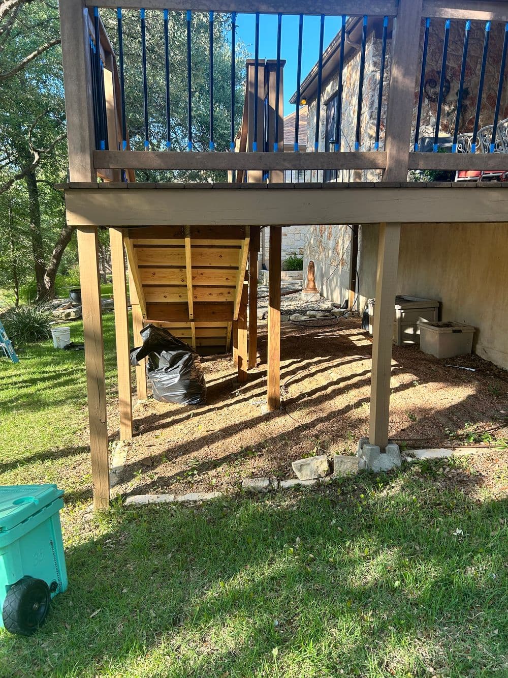 Under deck storage area with wooden stairs, grass, and a hint of shed in the background.
