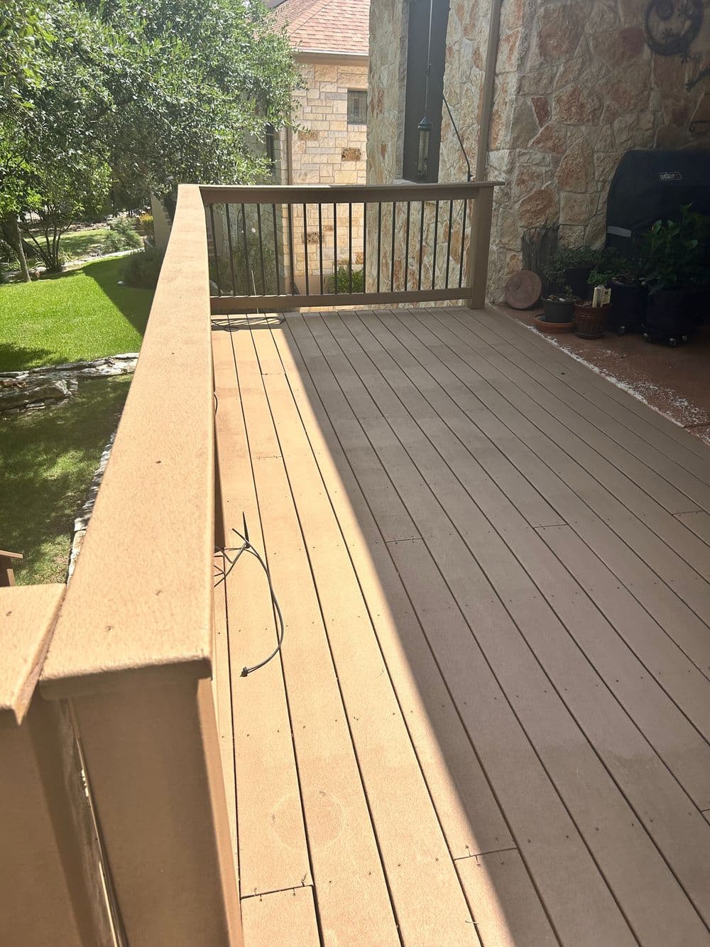 Wooden deck with sunlight casting shadows, surrounded by greenery and stone walls.