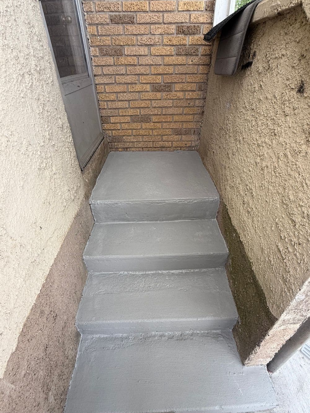 Freshly painted gray concrete stairs leading to a brick wall entrance.