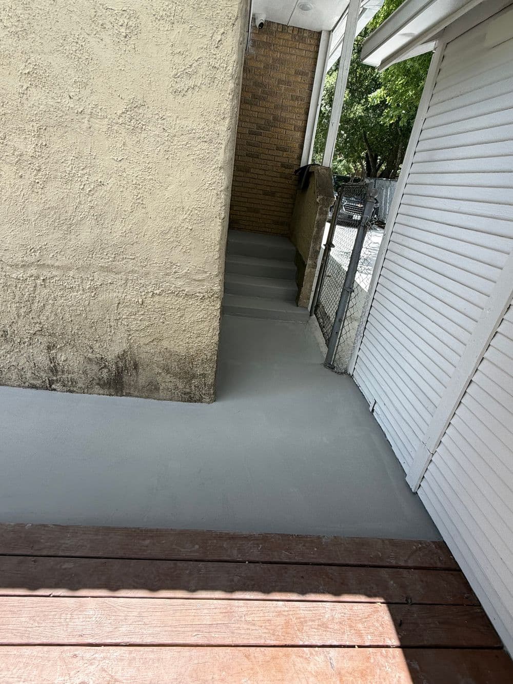 Freshly poured gray concrete pathway beside a house, leading to a gated area.