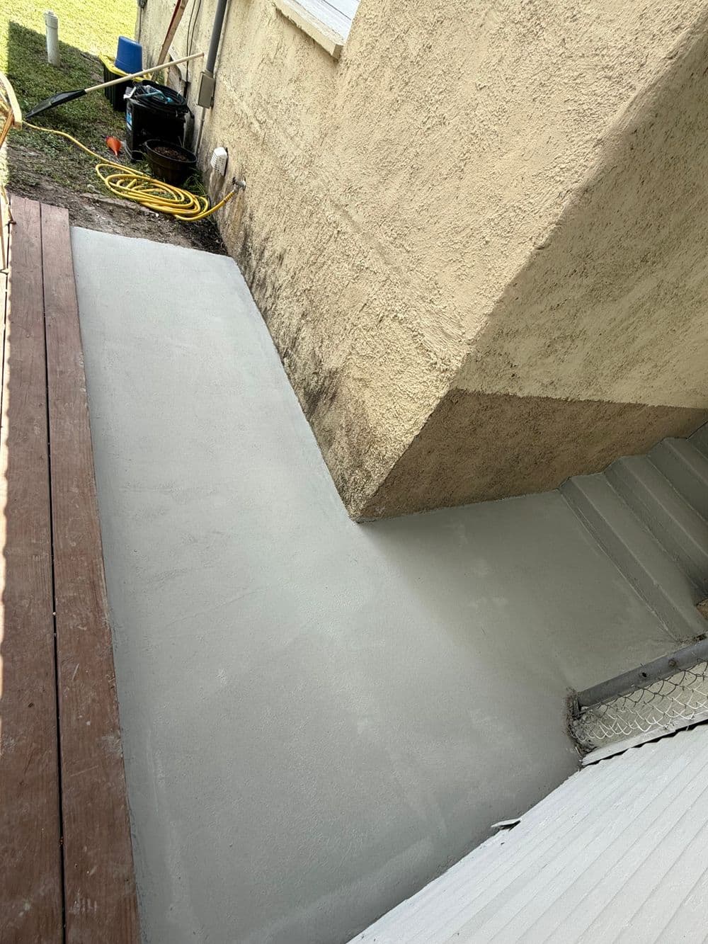Freshly poured concrete walkway beside a house near stairs and wooden deck.